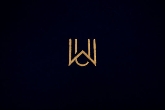 WAKE Monogramm in Gold auf schwarzem Oversized T-Shirt – Stickdetail Vorderseite