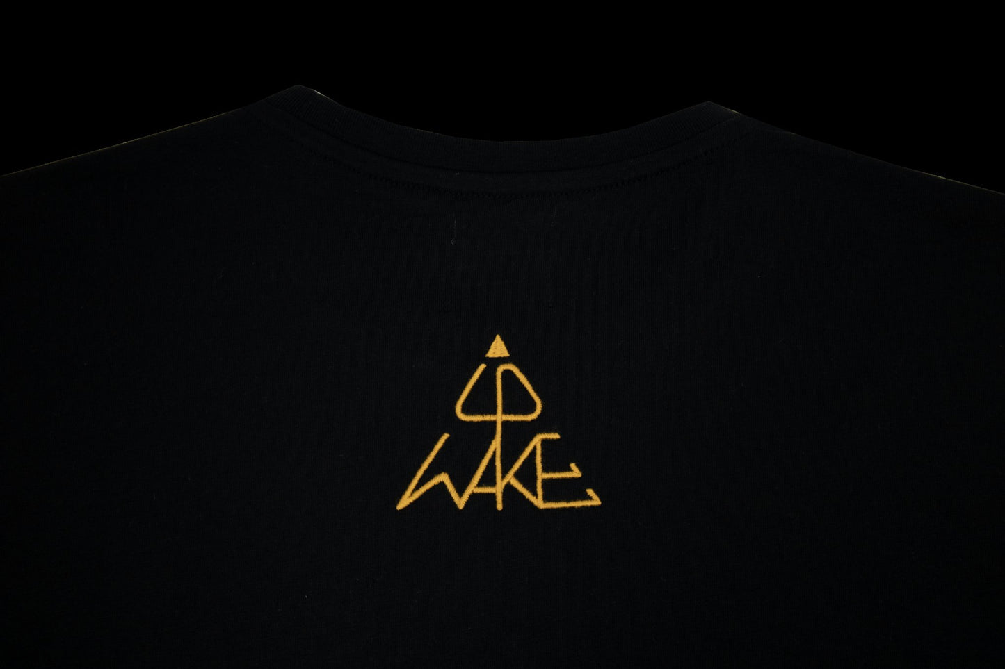 Pyramidenförmige WAKE UP Wortbildmarke – goldene Stickerei auf Oversized-Shirt Rückseite