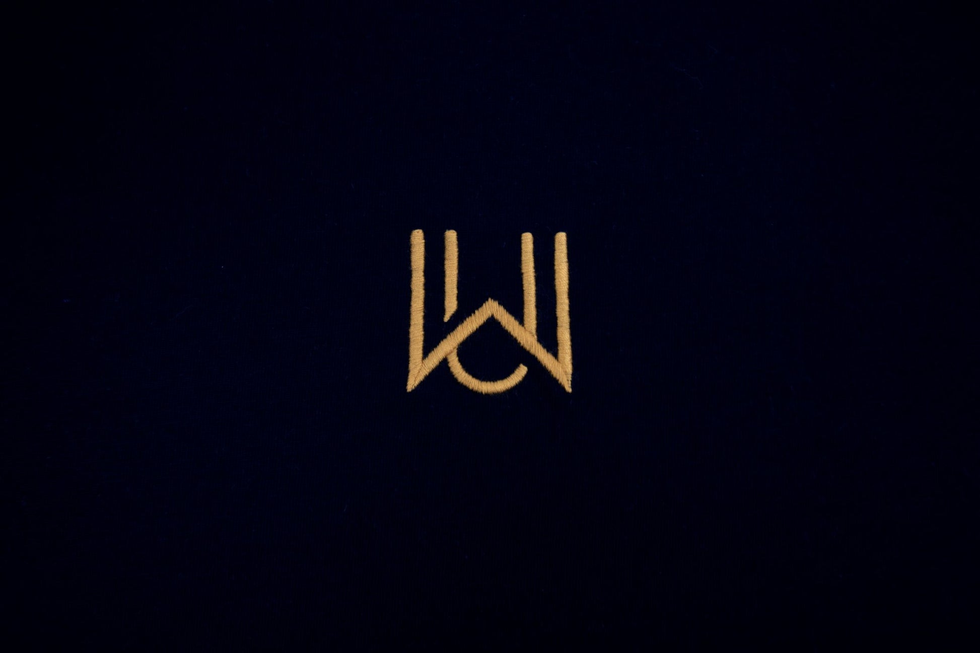 WAKE Monogramm in Gold auf schwarzem Oversized T-Shirt – Stickdetail Vorderseite